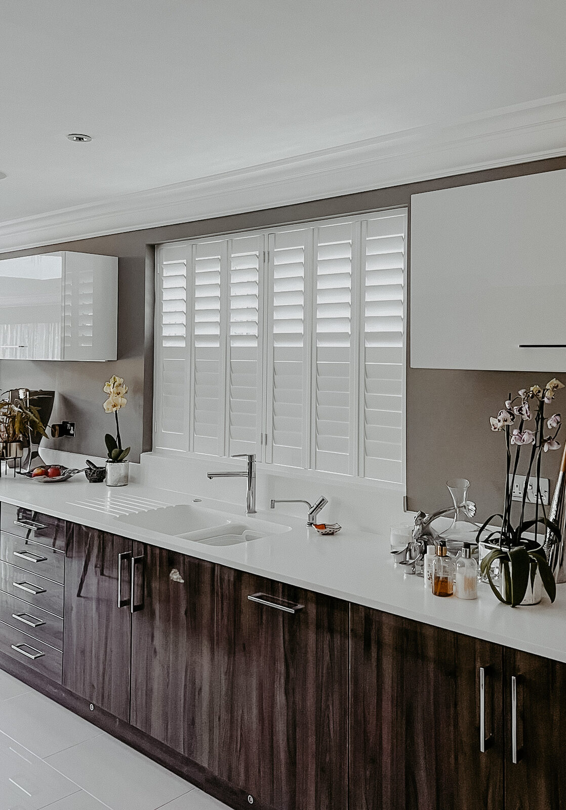 Shutters above a kitchen sink in a dark gloss kitchen